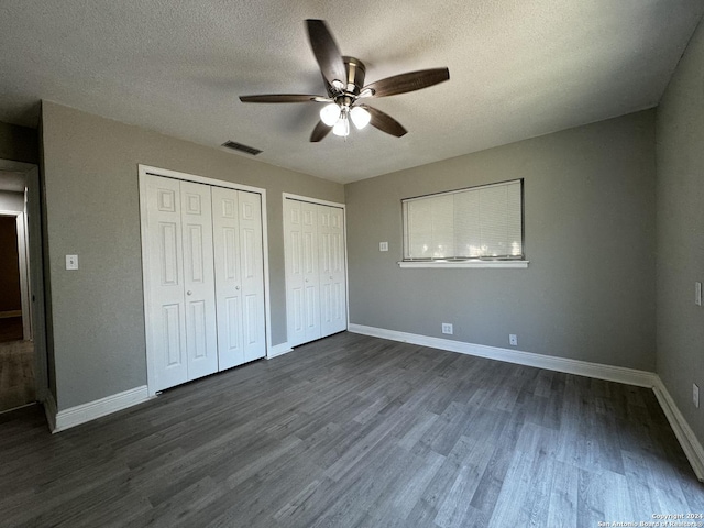 unfurnished bedroom featuring a textured ceiling, ceiling fan, dark wood-type flooring, and two closets