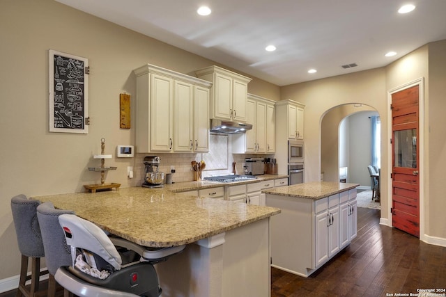 kitchen featuring light stone countertops, appliances with stainless steel finishes, a kitchen bar, tasteful backsplash, and a center island