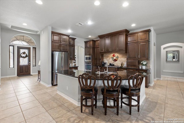 kitchen with sink, an island with sink, light tile patterned floors, and appliances with stainless steel finishes