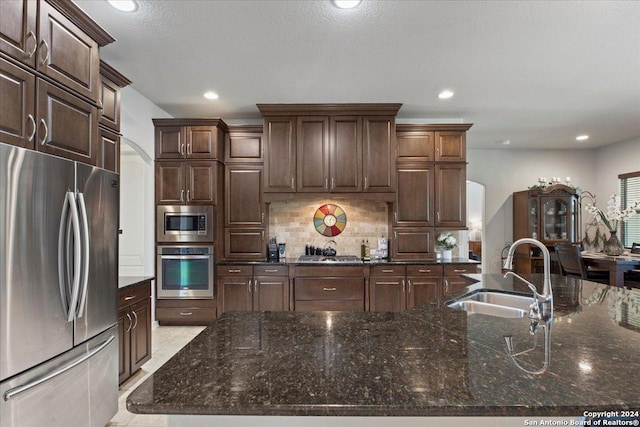 kitchen featuring decorative backsplash, appliances with stainless steel finishes, dark brown cabinets, a kitchen island with sink, and sink