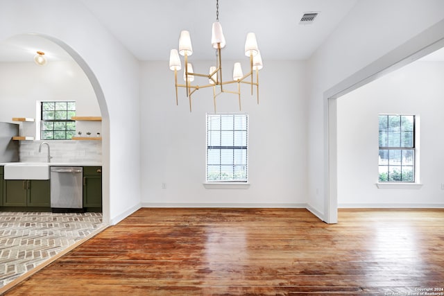 unfurnished dining area with a notable chandelier, sink, plenty of natural light, and hardwood / wood-style floors