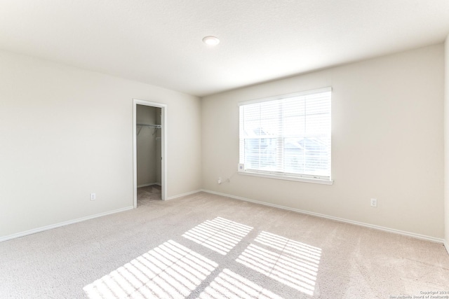 unfurnished bedroom featuring a walk in closet, light colored carpet, and a closet