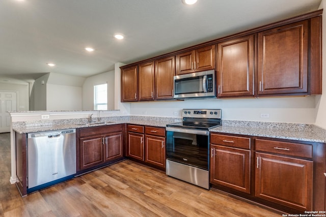 kitchen featuring sink, light stone counters, vaulted ceiling, hardwood / wood-style flooring, and stainless steel appliances