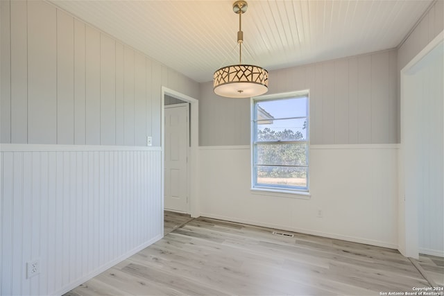 unfurnished room with light wood-type flooring and wooden walls