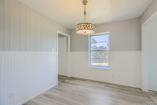 unfurnished room with light wood-type flooring and wooden walls