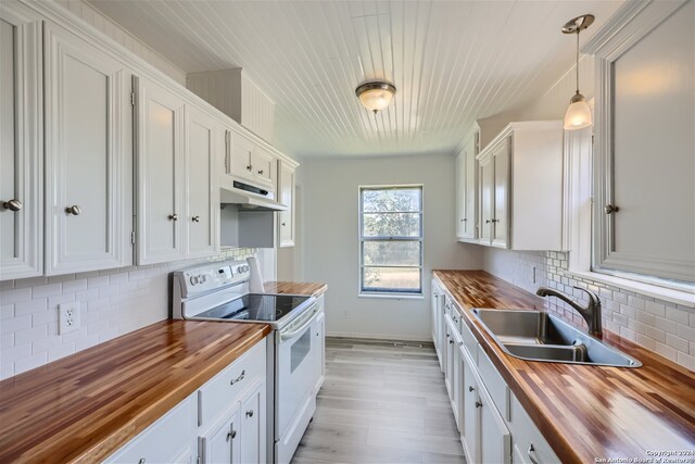 kitchen featuring white electric range oven, sink, white cabinetry, hanging light fixtures, and butcher block counters