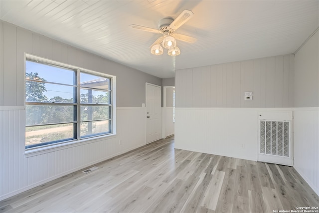 unfurnished room featuring light wood-type flooring, ceiling fan, and wooden walls