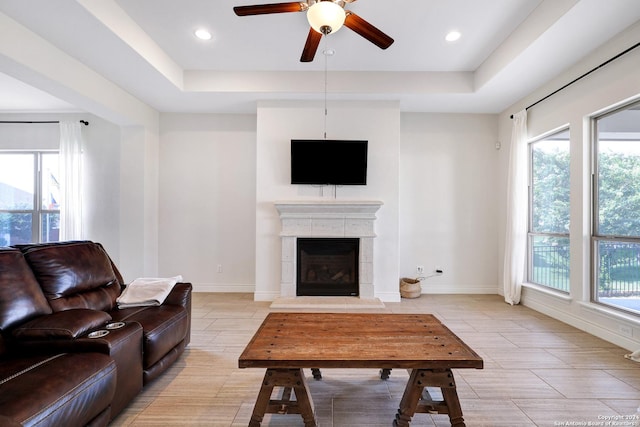 living room featuring a tile fireplace, a raised ceiling, and a healthy amount of sunlight