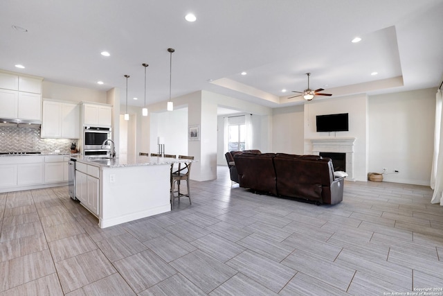 kitchen with a kitchen island with sink, sink, hanging light fixtures, ceiling fan, and light stone countertops