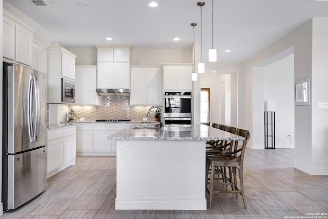 kitchen with appliances with stainless steel finishes, light stone counters, a kitchen island with sink, sink, and decorative light fixtures