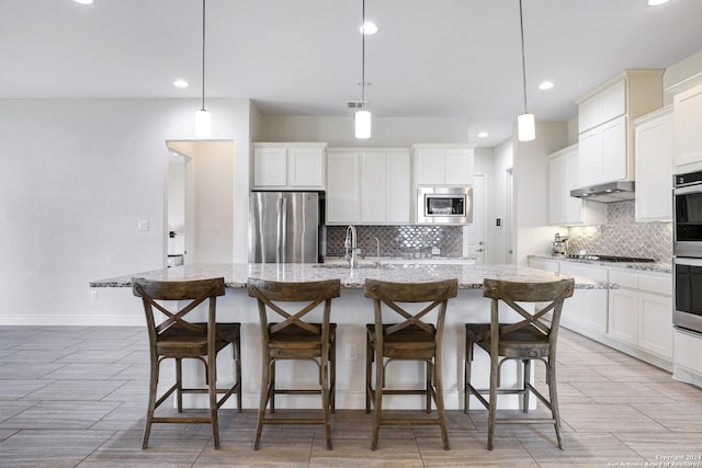 kitchen with a kitchen bar, a kitchen island with sink, hanging light fixtures, and appliances with stainless steel finishes