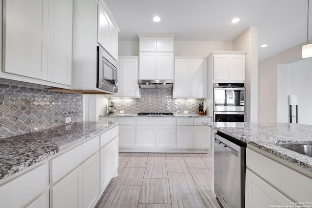 kitchen featuring white cabinets, hanging light fixtures, decorative backsplash, appliances with stainless steel finishes, and light stone counters