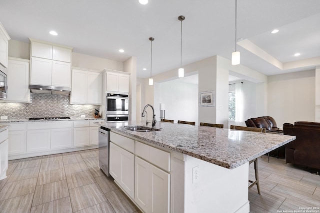 kitchen featuring a breakfast bar, backsplash, a center island with sink, sink, and decorative light fixtures