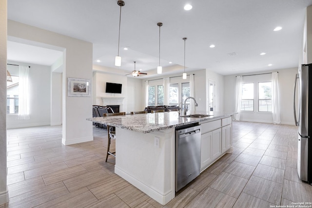 kitchen with light stone countertops, stainless steel appliances, pendant lighting, a center island with sink, and white cabinets