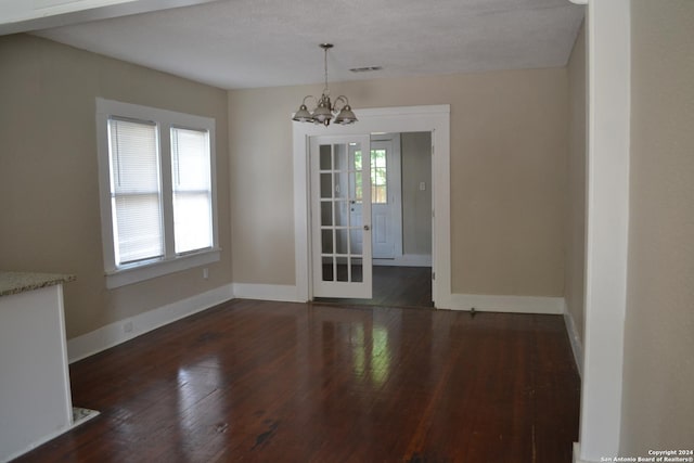 unfurnished dining area featuring a chandelier, french doors, a textured ceiling, and dark wood-type flooring