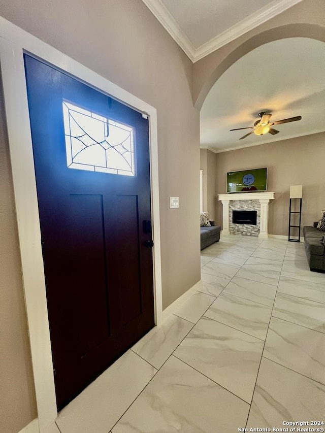 entrance foyer featuring a stone fireplace, ceiling fan, and ornamental molding