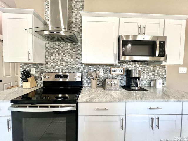 kitchen featuring light stone counters, white cabinetry, stainless steel appliances, and wall chimney range hood