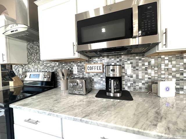 kitchen with white cabinets, wall chimney range hood, backsplash, and appliances with stainless steel finishes