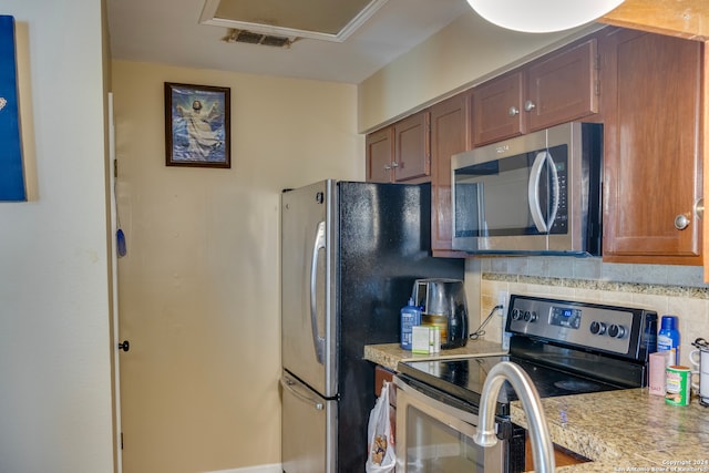 kitchen with visible vents, brown cabinets, stainless steel appliances, light countertops, and decorative backsplash