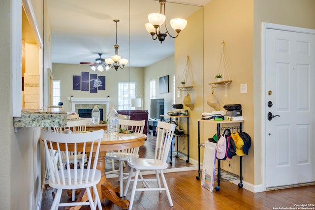 dining space featuring baseboards, hardwood / wood-style floors, a fireplace, and ceiling fan with notable chandelier