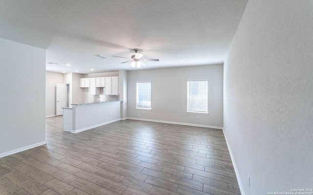 unfurnished living room with baseboards, a textured ceiling, a ceiling fan, and light wood-style floors