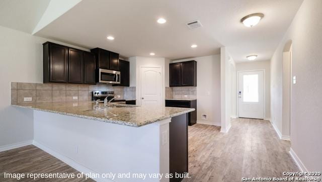 kitchen with kitchen peninsula, backsplash, stainless steel appliances, sink, and light hardwood / wood-style floors