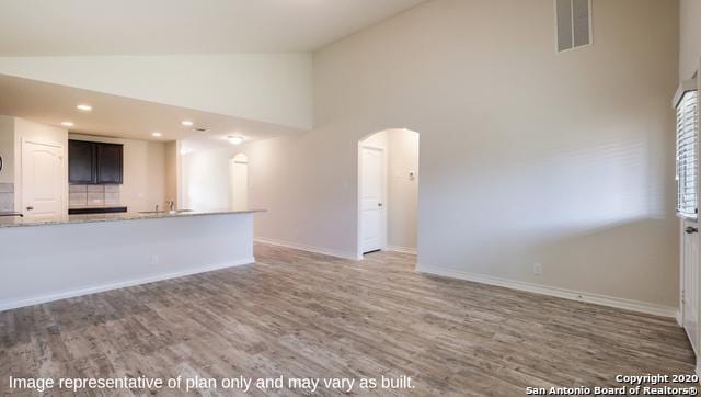 unfurnished living room featuring high vaulted ceiling and dark wood-type flooring