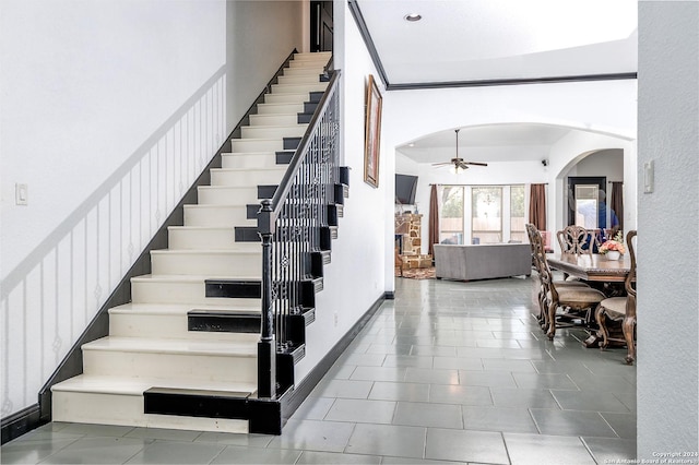 stairs featuring a stone fireplace and ceiling fan