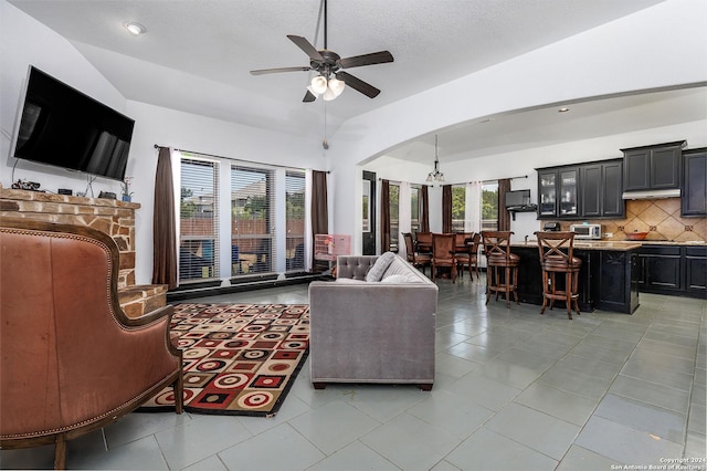 living room with lofted ceiling, plenty of natural light, ceiling fan with notable chandelier, and light tile patterned floors