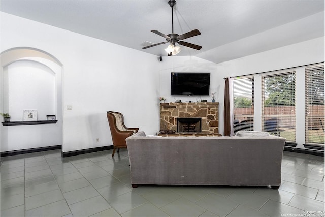 living room with tile patterned flooring, vaulted ceiling, a stone fireplace, and ceiling fan