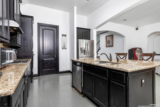 kitchen featuring light stone countertops, appliances with stainless steel finishes, sink, and a center island with sink