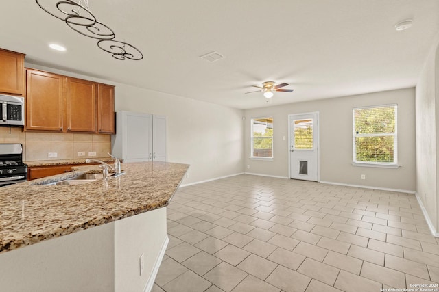 kitchen featuring backsplash, sink, light stone countertops, plenty of natural light, and stainless steel appliances