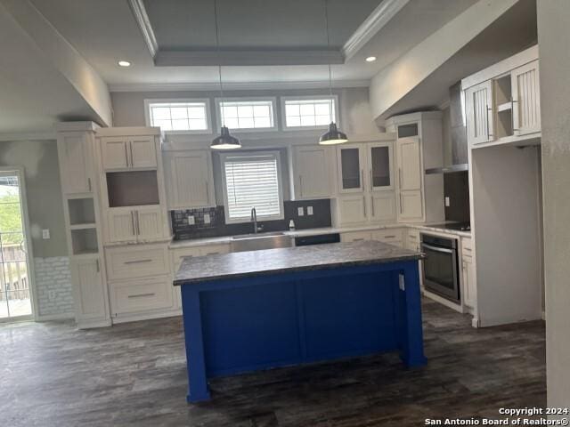 kitchen with a raised ceiling, pendant lighting, white cabinets, a center island, and oven