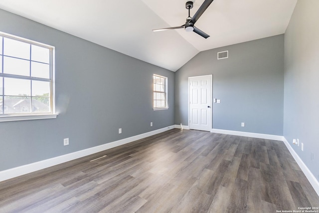 empty room featuring ceiling fan, vaulted ceiling, plenty of natural light, and dark wood-type flooring