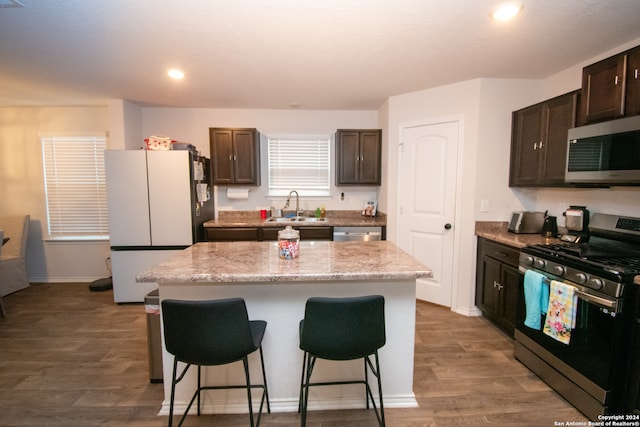 kitchen featuring stainless steel appliances, a center island, dark brown cabinets, wood-type flooring, and sink