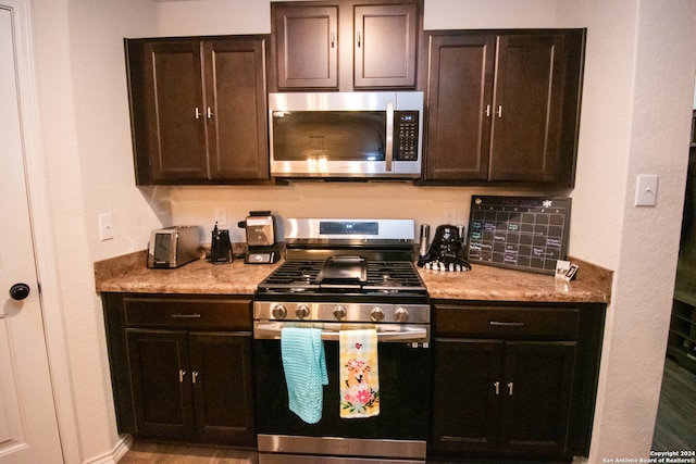 kitchen featuring light stone countertops, dark brown cabinets, light hardwood / wood-style flooring, and appliances with stainless steel finishes