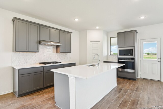 kitchen with sink, gray cabinetry, decorative backsplash, a kitchen island with sink, and stainless steel appliances