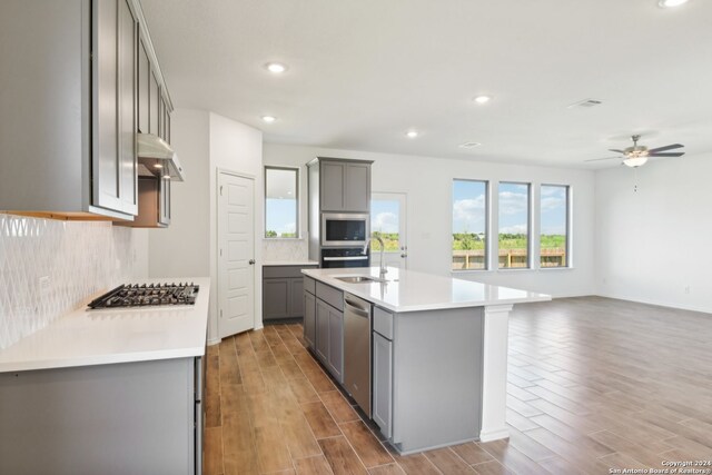 kitchen with sink, hardwood / wood-style flooring, a kitchen island with sink, gray cabinetry, and stainless steel appliances