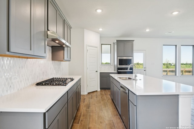 kitchen featuring sink, gray cabinets, stainless steel appliances, and an island with sink