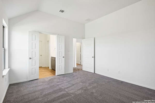 unfurnished bedroom with vaulted ceiling, light colored carpet, and ensuite bathroom