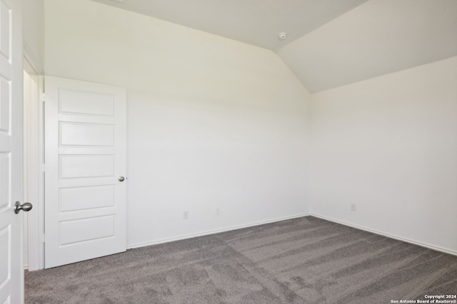 unfurnished room featuring lofted ceiling and dark carpet