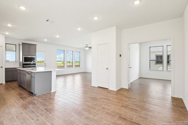 kitchen featuring sink, a center island with sink, light hardwood / wood-style flooring, appliances with stainless steel finishes, and ceiling fan