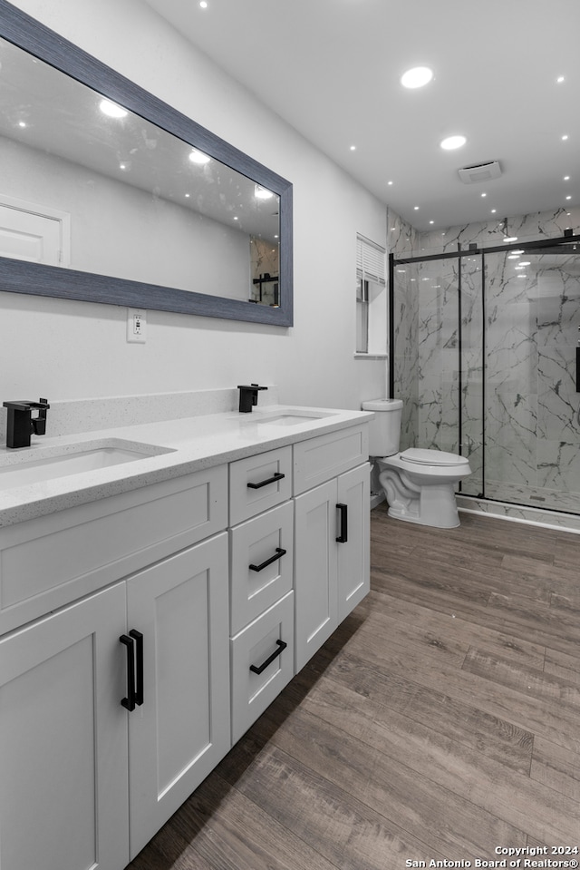 bathroom with dual bowl vanity, a shower with shower door, hardwood / wood-style flooring, and toilet