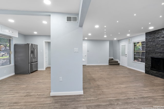 interior space with stainless steel fridge with ice dispenser, a stone fireplace, white cabinetry, and hardwood / wood-style flooring