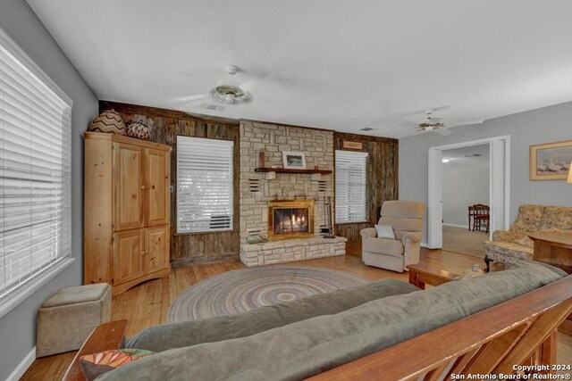 living room with a stone fireplace, ceiling fan, a healthy amount of sunlight, and light wood-type flooring