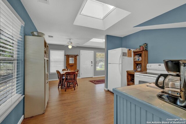 kitchen with a skylight, ceiling fan, light wood-type flooring, tile counters, and white appliances