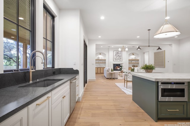 kitchen with a sink, stainless steel appliances, light wood-style floors, white cabinets, and hanging light fixtures