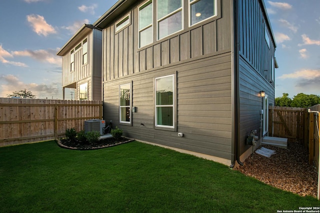 rear view of property featuring a lawn and central air condition unit