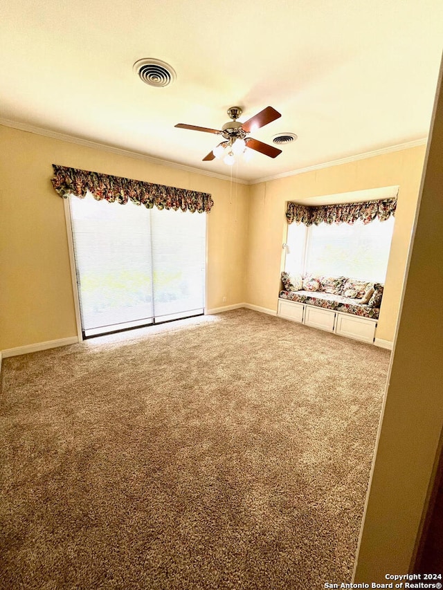 carpeted spare room featuring a healthy amount of sunlight, ornamental molding, and ceiling fan