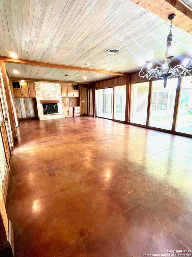 unfurnished living room featuring concrete flooring, a large fireplace, a chandelier, and wooden ceiling